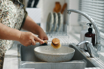 Close-up of housewife using brush to wash dirty pan in sink in the kitchen