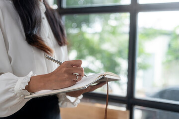 Businesswoman writing notes in notebook by office window