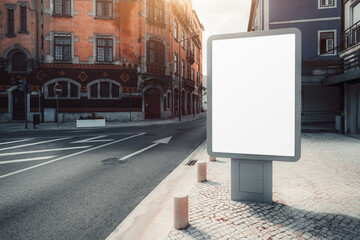 A blank billboard mockup stands on a cobblestone street in front of a historic building with red-orange facade. The billboard is empty, ready for advertisement placement, with sunlight casting shadows
