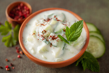Indian Fresh sauce called Raita with herbs, dahi and sliced cucumber in a bowl on the table.