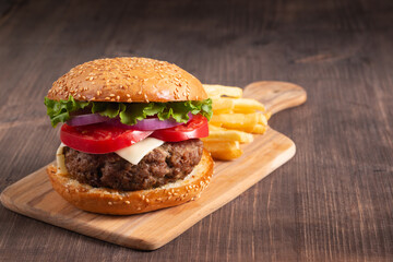 Homemade delicious hamburger with beef, onion, tomato, lettuce and cheese. Fresh burger close up on wooden rustic table with potato fries. Cheeseburger. Burger.