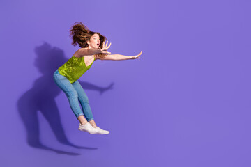 Obraz premium Full length photo of lovely teen lady jumping pushing invisible things dressed stylish green garment isolated on violet color background