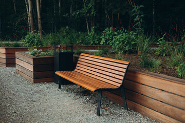 A modern wooden bench with black trash bin standing in the park. Comfortable bench in recreation area. City improvement, urban planning, public spaces.