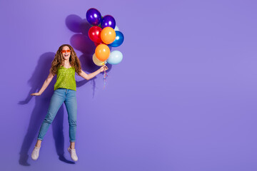 Full size photo of pretty teenager girl flying hold air balloons wear trendy green outfit isolated on purple color background