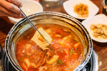 Chopsticks Picking Up Tofu from Kimchi Stew in a Metal Pot