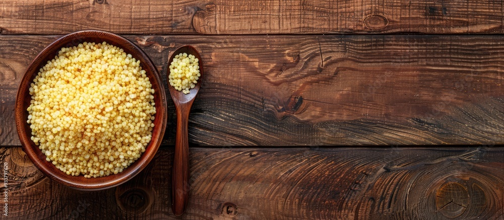Poster top-down view of a wooden table with a bowl and spoon containing raw bulgur, ideal for adding text i