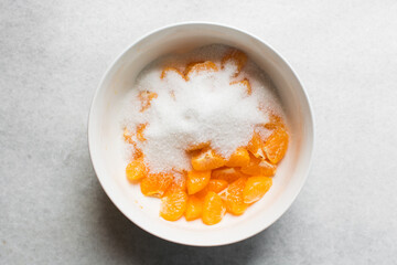 Overhead view of diced tangerine and sugar being mixed together in a white bowl, process of making tangerine cheong or tangerine syrup