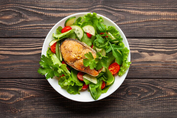 Fresh vegetable salad and baked salmon in a plate on the table. Mediterranean diet concept. Top view