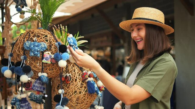 Beautiful Young Woman in a Linen Green Shirt and Straw Hat Picks Out Handmade Souvenirs at the Weekend Jing Jai Market, Having Fun. Vacation, Asian Culture, Shopping Concept