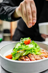 Close-up of hands garnishing a fresh salad with grilled tuna, vegetables, and greens in a white bowl.
