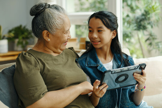 Girl using tablet pc and talking to her grandmother while they sitting on sofa in the living room