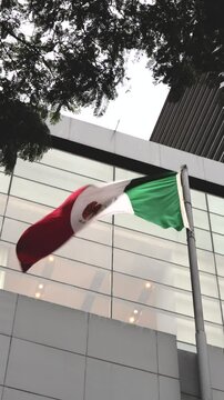 Bandera de M&eacute;xico ondeando con edificios atr&aacute;s