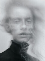 A portrait of a woman with blonde hair, wearing a black top, with her hair blowing upwards, creating a blurred effect.