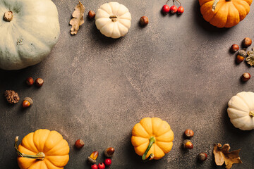 Frame of ripe orange pumpkins, fallen leaves, red berries, nuts on stone background. Autumn, fall concept.