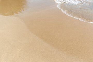 Small wave on a smooth sandy beach on a sunny day, viewed from above. Natural tropical travel, vacation and summer background with copy space.