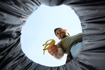Man throwing banana peel into garbage bin outdoors, bottom view