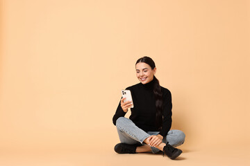 Smiling woman with smartphone on beige background. Space for text