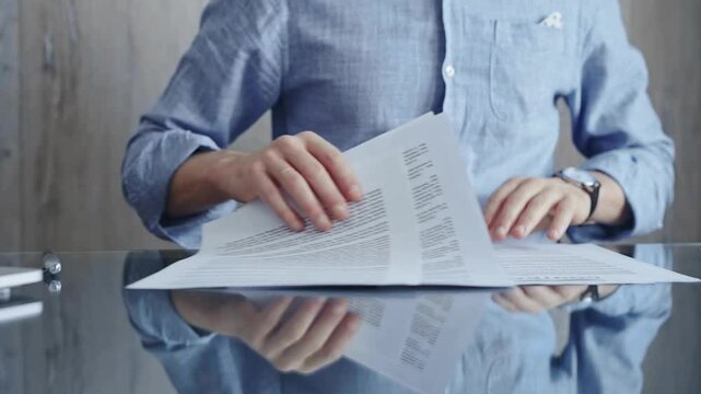 Businessperson analyzing document at desk. Close-up of a professional auditor or lawyer reviewing a lengthy paper report in office setting. Business people concept