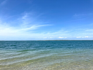 An serene ocean on a summer's day, against a background of a blue sky, and wisps of clouds.
