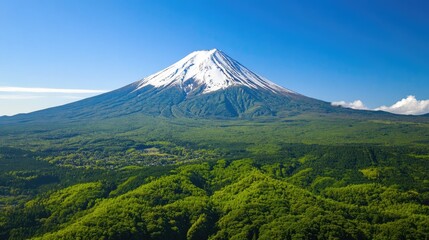 Fototapeta premium Aerial view of Japan's iconic Mount Fuji surrounded by lush green forests and clear blue skies.