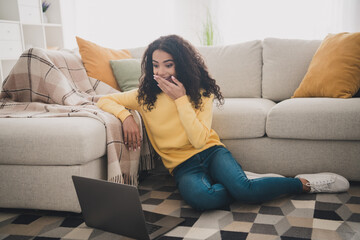 Obraz premium Photo of curly hair young funny girl close mouth surprised sitting floor with laptop watching comedy series indoors living room apartment