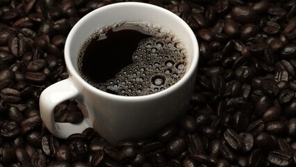 Top view of coffee or espresso with piles of coffee beans. Close up of fresh roasted coffee bean scatter around wooden table with cup of americano and aromatic stream and smoke from seed. Comestible.