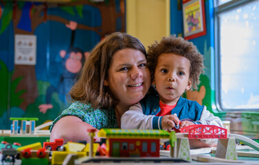 Mom and child play with a train set at nursery, kinder garden. Multi ethnic boy and mother at...