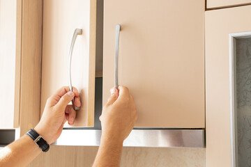 Male hands opening beige kitchen cabinet in kitchen in apartment