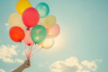 Naklejka premium Bright balloons floating against a clear blue sky with fluffy clouds, creating a joyful and whimsical atmosphere.