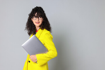 Obraz premium Beautiful young woman in stylish yellow suit with laptop on grey background, space for text