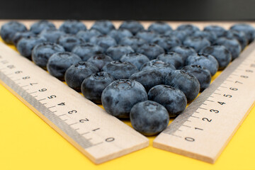 Fresh blueberry and wooden measuring rulers on yellow background	