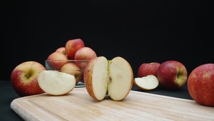 Macrography of apples displayed in various forms: whole, sliced, and within a glass bowl with black background. Each close-up shot captures the red colors of the apples on cutting board. Comestible.