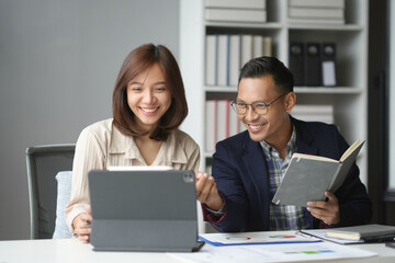 Two happy business partners are analyzing data on a digital tablet and discussing a project in a...