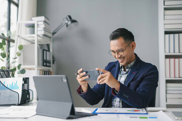 Businessman is smiling while taking a photo of his tablet with his phone, in his modern office
