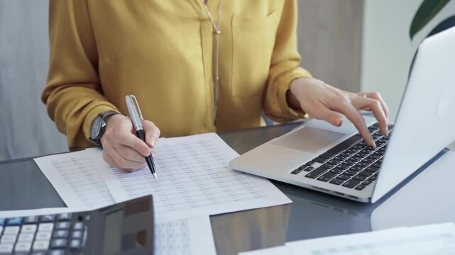 Professional business woman in yellow blouse is working on financial reports. Close-up of a woman's hands as she works on finance documents and laptop computer. Audit