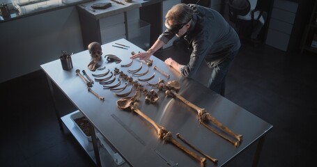 Archaeological laboratory: High angle of mature archaeologist in AR headset studying remains of...