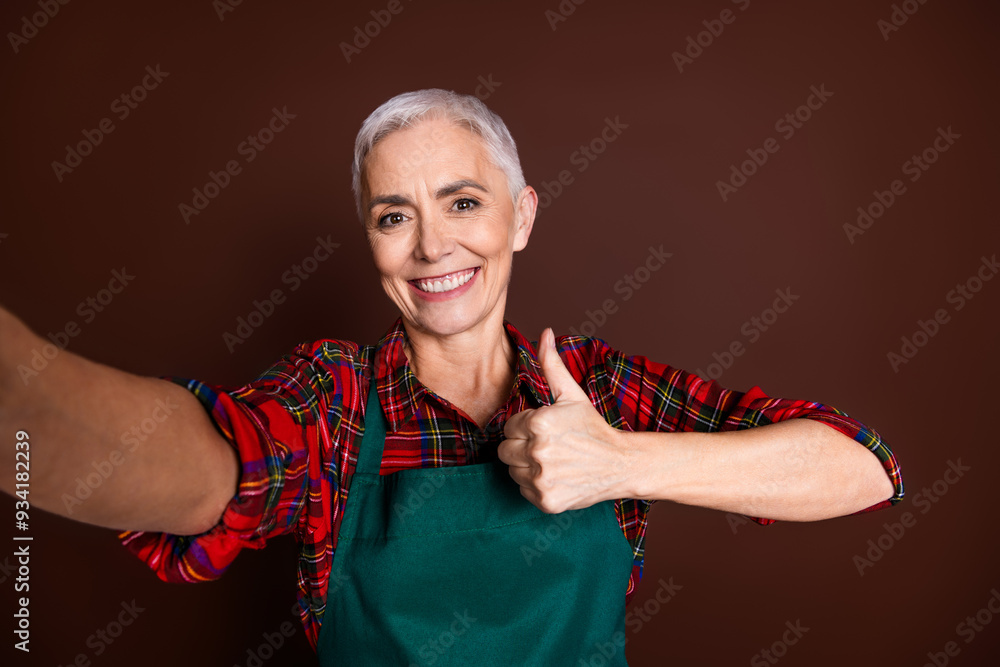 Poster Photo of lovely senior nice lady wear red checkered shirt take picture thumb up isolated on brown color background