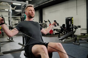 Bodybuilder having heavy workout in gym, he using horizontal pull machine