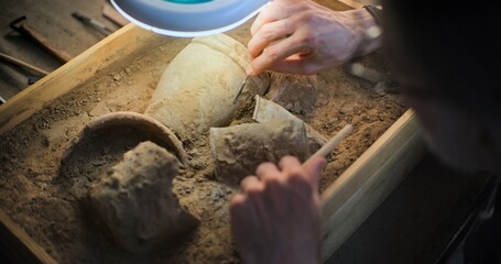 Close up of mature archaeologist cleaning cultural heritage of extinct civilization from sand under...