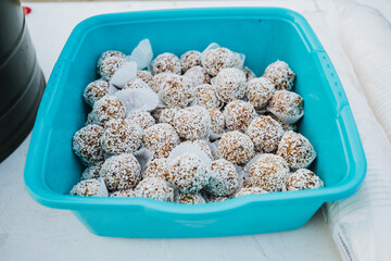 A blue plastic container is filled to the brim with circular coconut balls, showcasing a delightful snack that is both tasty and visually appealing, ideal for every occasion