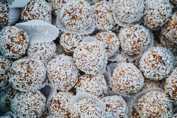 In this image, we see a detailed closeup view of a delightful pile of coconut balls elegantly arranged on a wooden table, showcasing their texture and the natural beauty of the ingredients