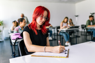 Fototapeta premium Focused young student taking notes from books for her study. College student sitting at desk and studying.