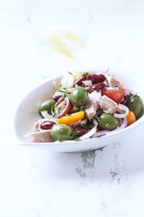 Salad with tuna, green olives and cherry tomatoes. Bright wooden background. Close up. Copy space.	