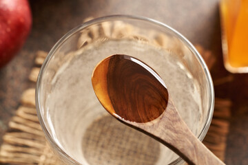 Apple cider vinegar on a wooden spoon with a glass of water