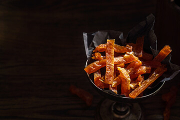 Jerky pork chips in vintage bowl close-up with black copy space. Dried meat slices
