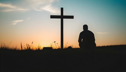 Silhouette of man kneeling near the wooden Christian cross on a nature meadow grass field outdoor at sunset