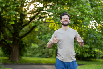 Smiling man gives thumbs up in a sunny park setting, showcasing positivity and healthy lifestyle...