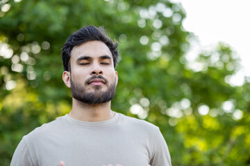 Young man practicing mindfulness and relaxation in outdoor nature setting with eyes closed, focusing on breathing techniques