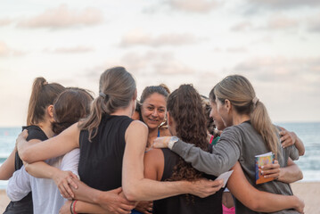 An intimate circle of friends share a warm embrace on the beach, their bond illuminated by the soft evening light reflected in calm waters