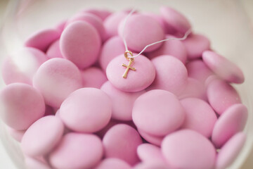 A golden pendant cross on the background of pink strawberry candies. baby shower